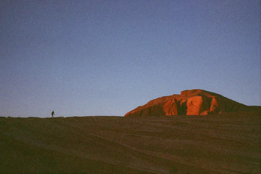 A small figure walking in the desert at sunset.