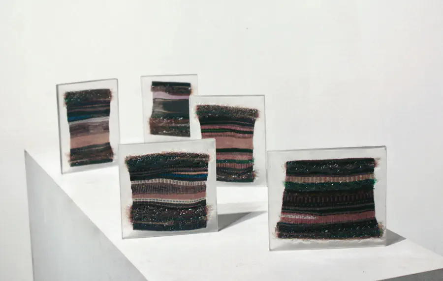 A series of knitted yarn swatches with pink and teal and white thread. Each of the five swatches are contained within resin.