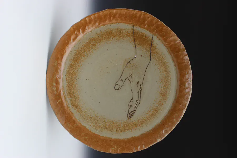 Plate with a bronze rim that depicts a hand reaching out.