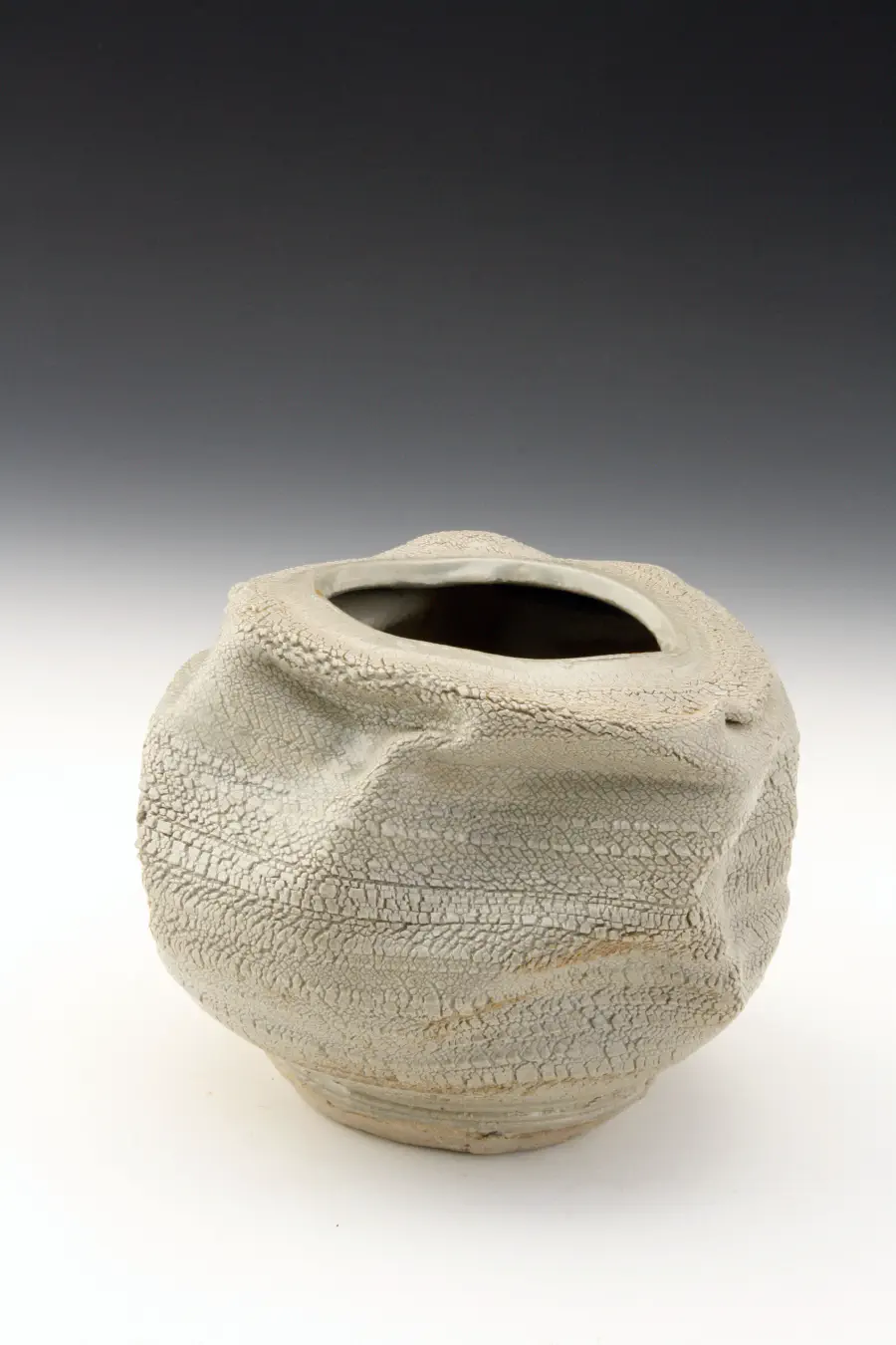 A textured creamy white vase that looks as if it's crumpled. The background is a gradient of black to white.
