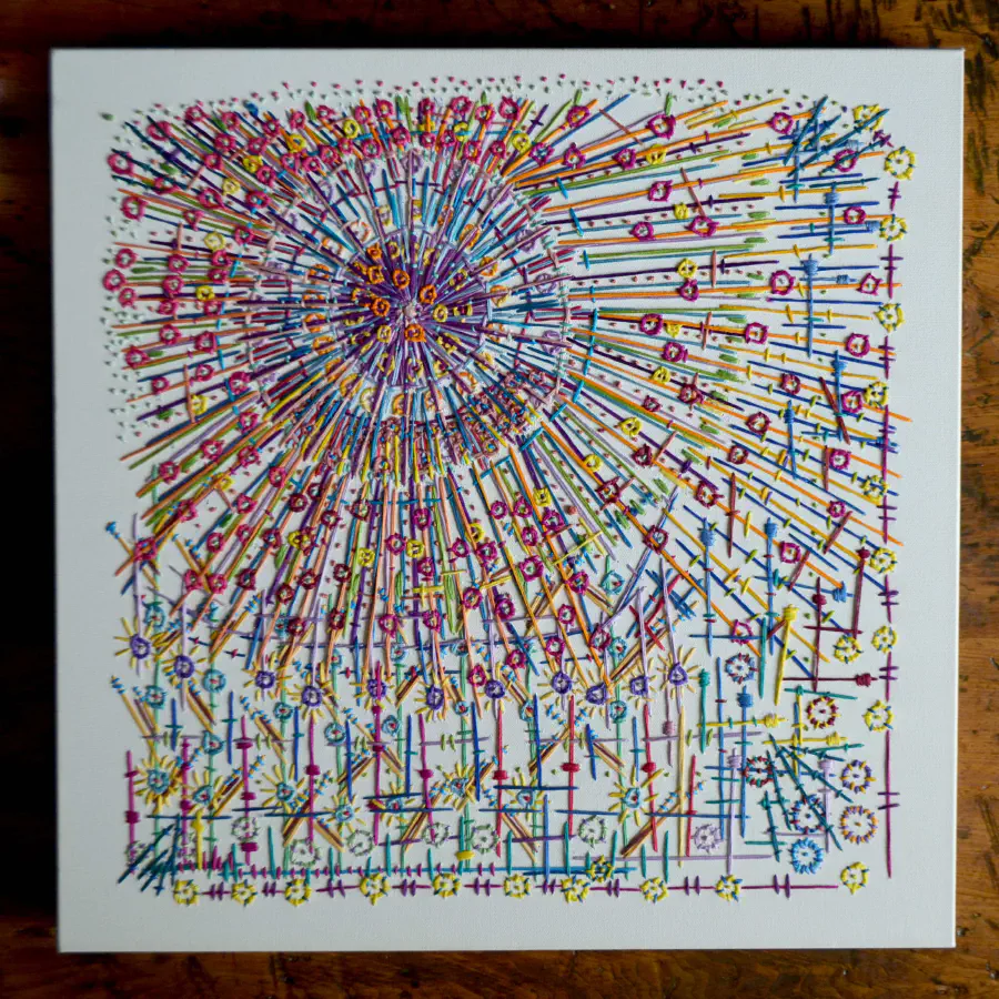 Embroidered abstract scene with colorful thread. A circular shape with mini circles surrounding a larger circle give way to criss crossed lines. It almost looks like a sun shining on people.